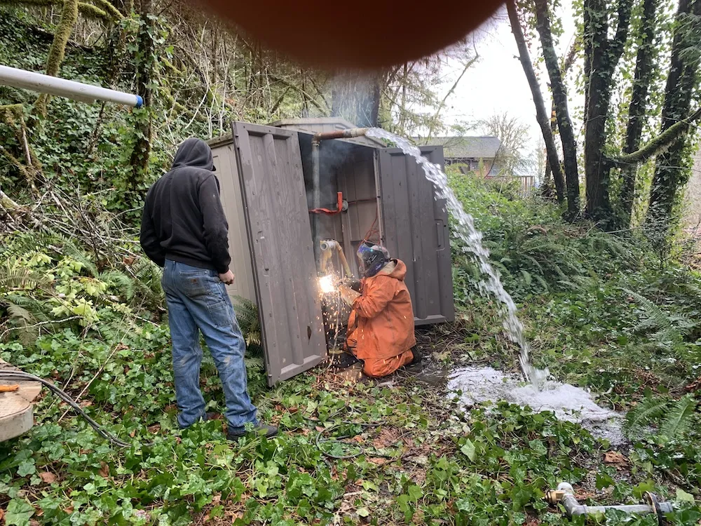 Welder working on a borehole as artesian water flows